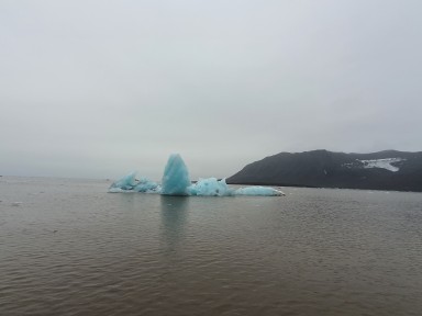 Isfjell med grønblå farge stikk opp av fjord i nord, tåkete himmel