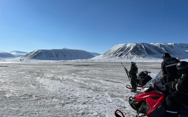 Svalbard i sol og blå himmel med snø og skuter i forgrunnen. Fjell bak