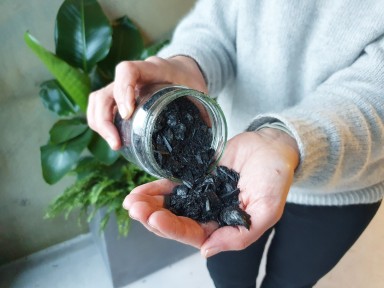 Kvinnehender med glas som inneheld svart biokol