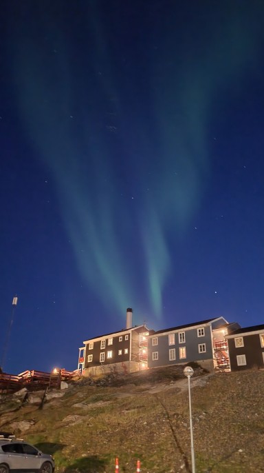 Trehus med mørk himmel over, på Grønland, grønt nordlys på den blå nattehimmelen.